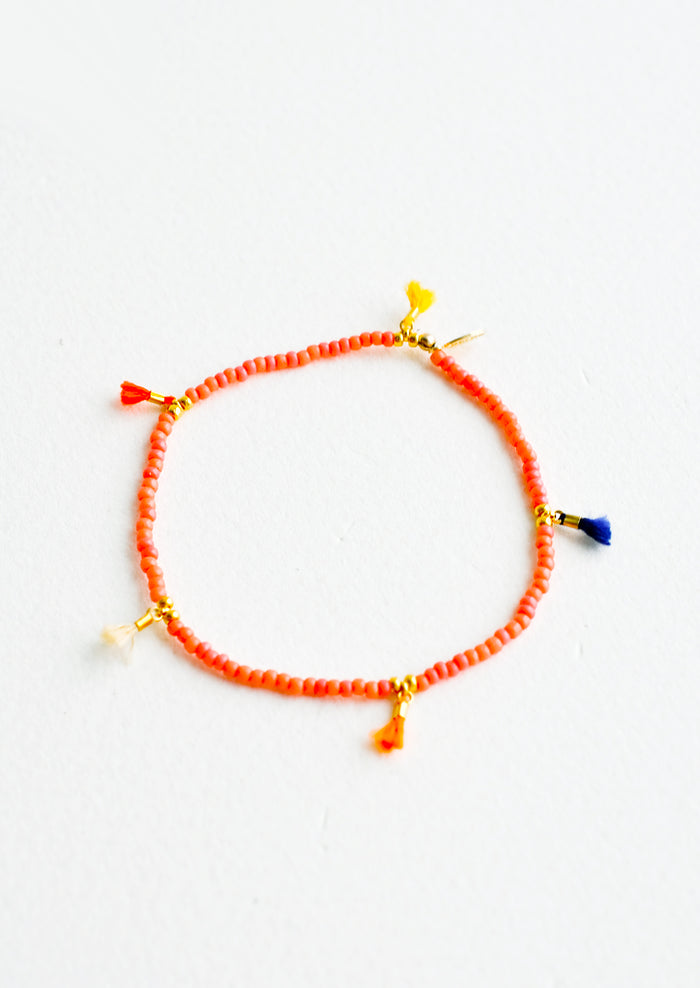 Bracelet featuring red beads interspersed with 5 small multicolor string tassels on an elastic cord.