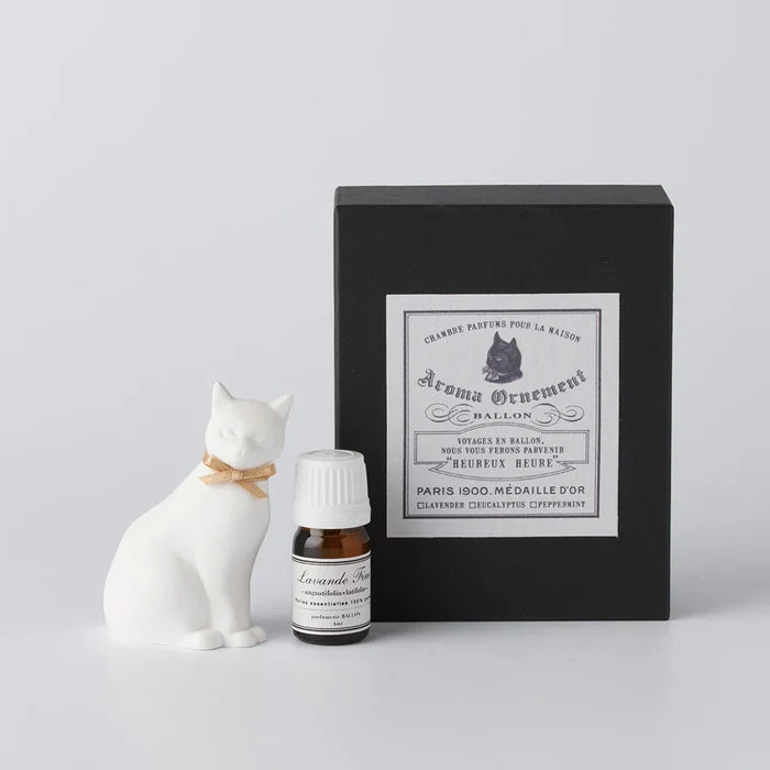 White cat-shaped aroma ornament gift set with a gold ribbon collar, essential oil bottle, and black vintage-style box, displayed on a clean white background in a minimalist home fragrance product presentation.