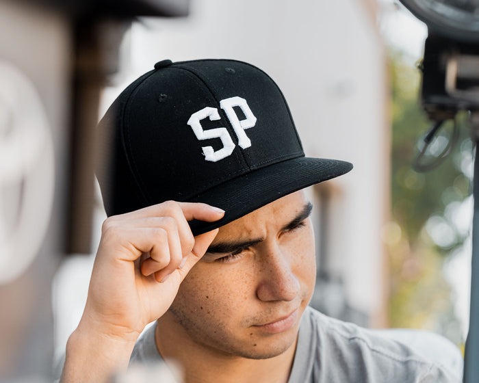 man wearing - black suavecito hat with white embroidered text "SP"