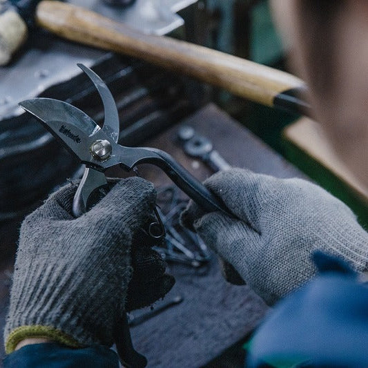 Person wearing gloves holding a pair of shears over a workbench with tools in the background