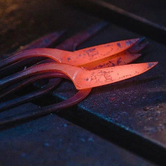 A close-up of glowing hot metal tools or bars resting on a dark workbench, with one piece illuminated in bright orange-red heat.