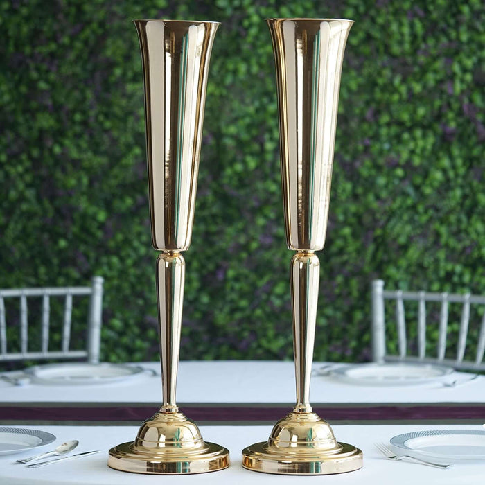 Elegant gold vases on a dining table with greenery backdrop.