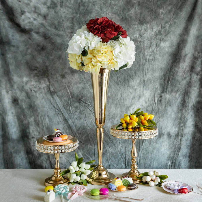 Elegant floral arrangements in gold vases with decorative sweets on a textured backdrop.