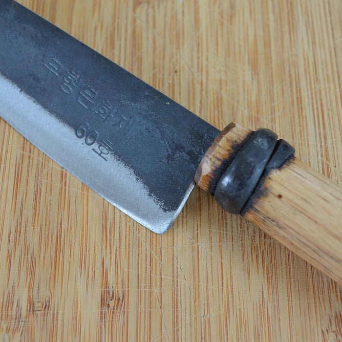Close-up of a small hand-forged kitchen knife with a dark steel blade and wooden handle, shown on a bamboo cutting board to highlight artisan craftsmanship and blade detail.