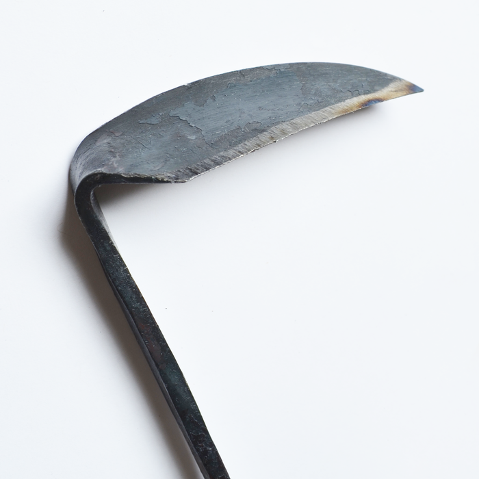 Close-up of a hand-forged small weeding hoe blade in dark steel, shown on a clean white background to highlight its curved shape, sharp edge, and artisan craftsmanship.