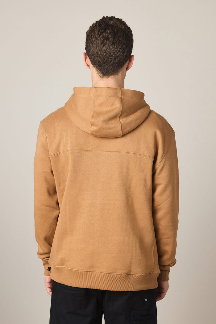 A person with short curly hair wears the 686 Men's All Season Hoody by 686 in tan, paired with black pants, standing with their back to the camera against a plain light background.