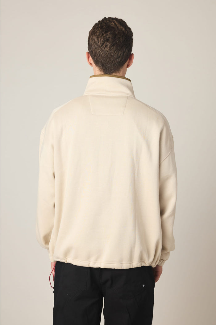 A person with short brown hair is standing with their back to the camera, wearing the 686 Men's Burnout Anorak in beige and black pants against a plain light background.