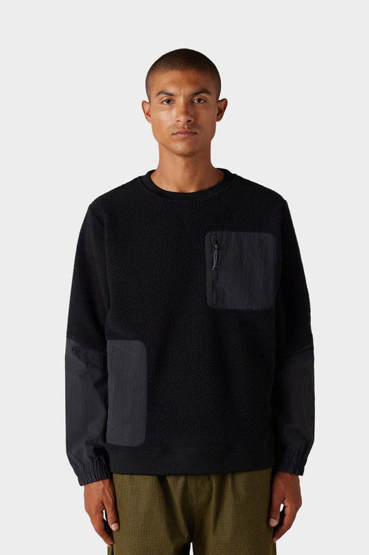 A person wearing the 686 Mens Buttermilk Sherpa Crew‚Äîa black textured long-sleeve sweatshirt‚Äîpaired with olive-green pants, stands against a plain light gray background.