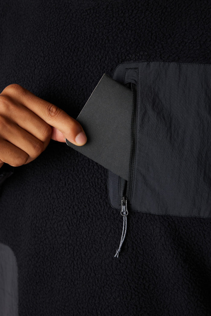 A hand slips a black card into the zippered chest pocket of the 686 Mens Buttermilk Sherpa Crew, blending comfort and style from 686 in one cozy fleece layer.