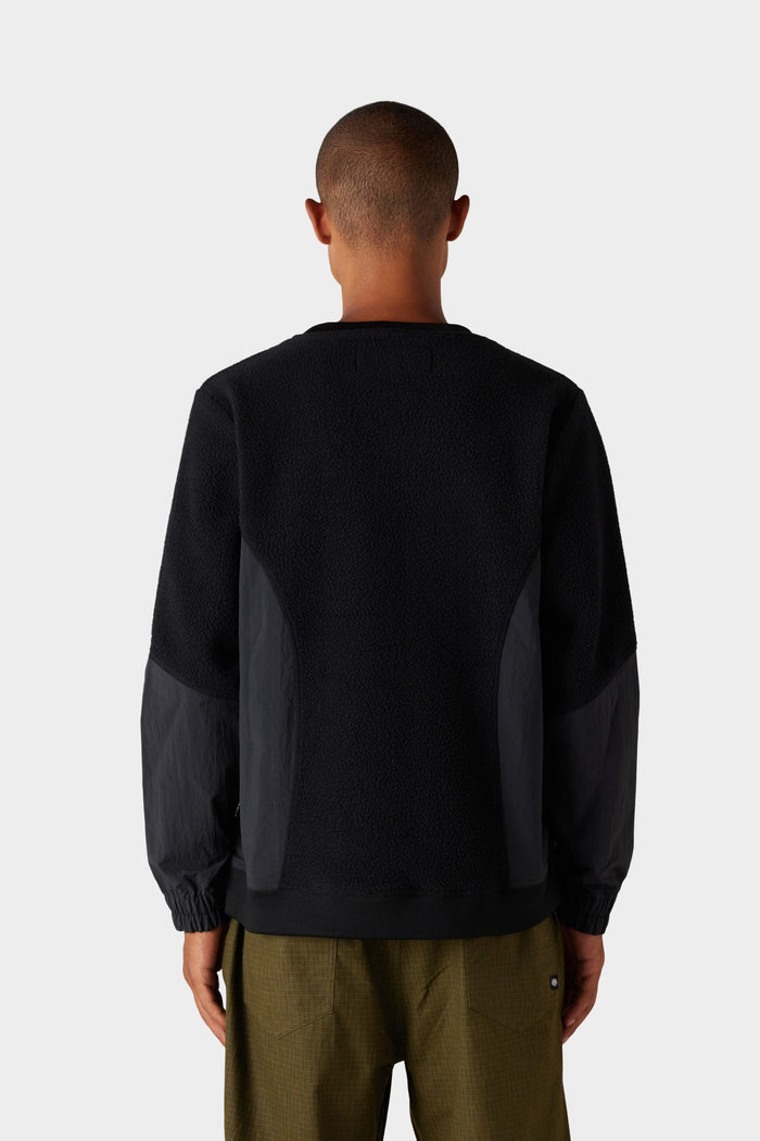 A person with short hair is seen from behind wearing the 686 Mens Buttermilk Sherpa Crew‚Äî a black textured sweater by 686‚Äîpaired with olive green pants. The background is plain and light gray.