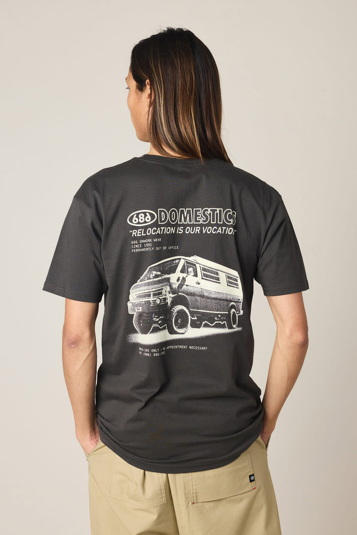A person stands with their back to the camera against a plain background, wearing the 686 Men's Domestics Authentic SS Tee—a black t-shirt from 686 made of 100% cotton, featuring a graphic of a van and the words "DOMESTIC RELOCATION IS OUR VOCATION" on the back.