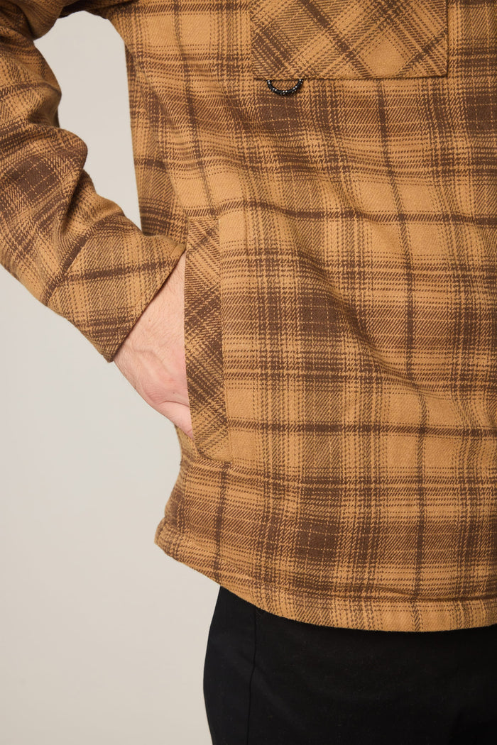 A person wearing the 686 Men's Heat Grid™ Flannel, with their left hand in a front pocket; the lower part of their torso and arm are visible, along with part of black pants.