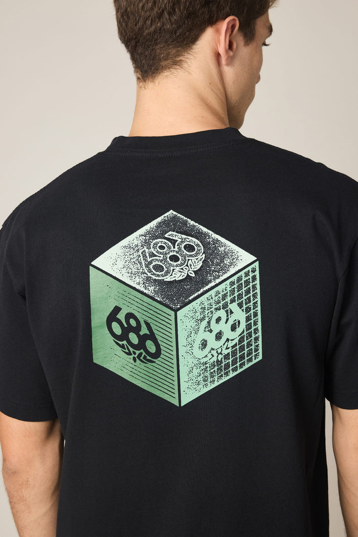 A person wearing the 686 Men's Unit Relaxed SS Tee by 686—a black 100% cotton T-shirt featuring a green and white cube graphic and the number 686 on the back.