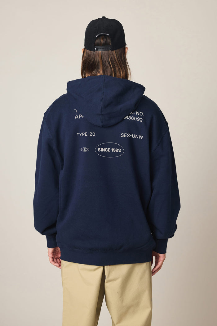 A person is facing away from the camera against a plain background, wearing the 686 Men's Unwork Spec Athletic LS Hoody by 686—a navy sweatshirt crafted from a comfortable cotton-spandex blend with white text and symbols on the back—paired with tan pants and a black cap.