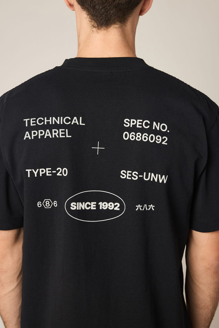 A person is seen from the back wearing the 686 Men's Unwork Spec Relaxed SS Tee by 686. The black, 100% cotton t-shirt features white printed text and symbols, including "TECHNICAL APPAREL," "TYPE-20," "SINCE 1992," and various codes.