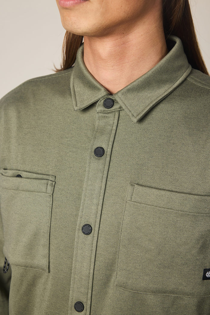 A person is shown from the shoulders to the chin wearing the 686 Men's Whisper Knit™ Flannel by 686—an olive green, 100% polyester shirt featuring two front pockets, black buttons, and a pointed collar.