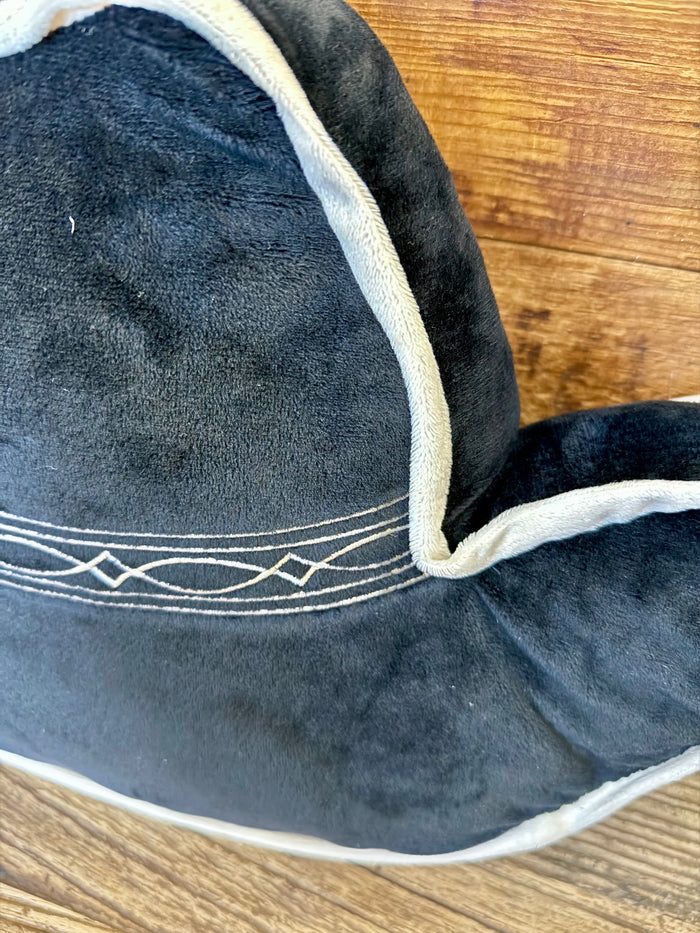Close-up of dark cowboy hat pillow with white piping and embroidered brim band