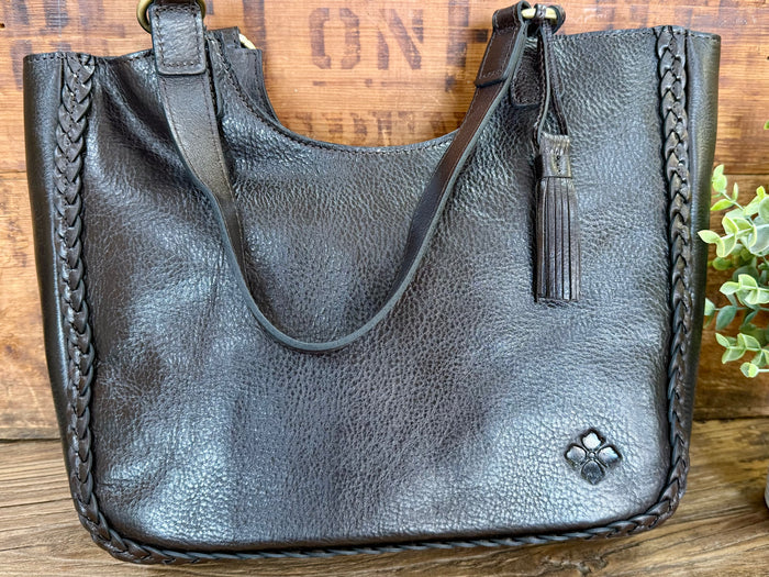 Dark brown leather tote with open top, braided side panels, and tassel detail at center