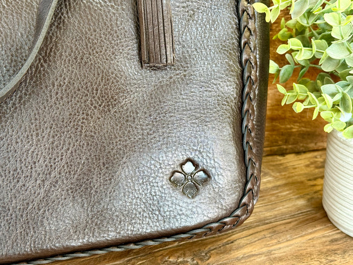 Close-up of dark brown leather tote front with small decorative logo and braided trim