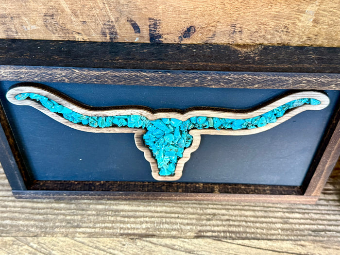 Wood framed turquoise longhorn silhouette on blue background, side view.