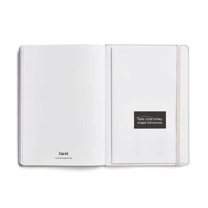 Inside view of Karst A5 Stone Paper Notebook showing blank stone paper pages, interior pocket with branded card, and elastic closure strap, displayed on a white background.