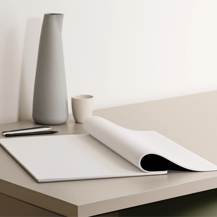 Minimalist desk setup with a vase, pen, and magazine on a light surface.