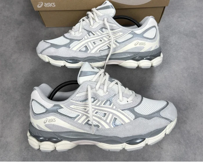 Pair of gray and white running shoes with a brown Asics box on a gray surface