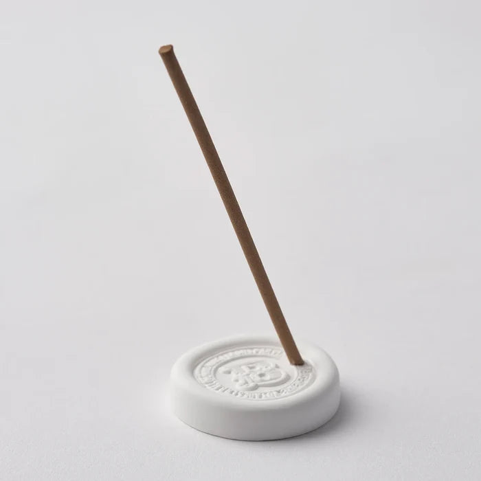 Ceramic incense holder with a single incense stick on a light gray background