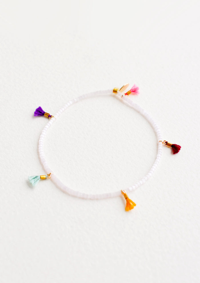 Bracelet featuring white beads interspersed with 5 small multicolor string tassels on an elastic cord.