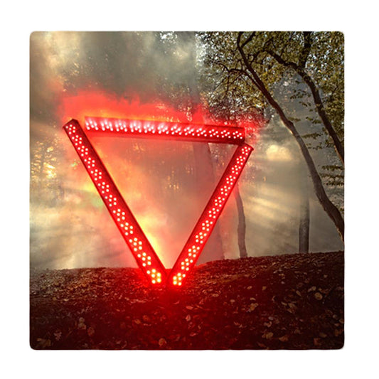 A glowing red, illuminated triangle stands upright in a misty forest—like a warning from the Enter Shikari system—as beams of sunlight stream through the trees in the background.