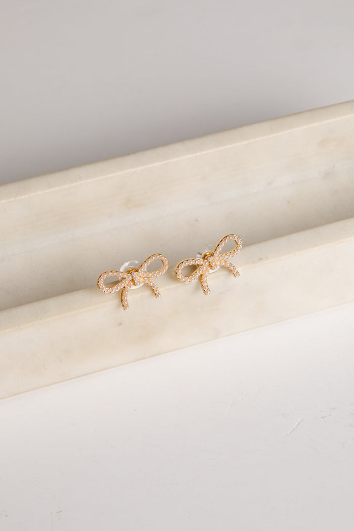 Gold bow-shaped earrings on a marble surface