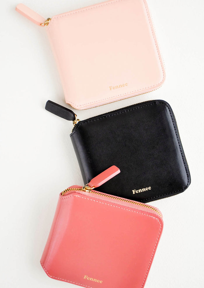 Three leather zip wallets in pale pink, black, and deep pink.
