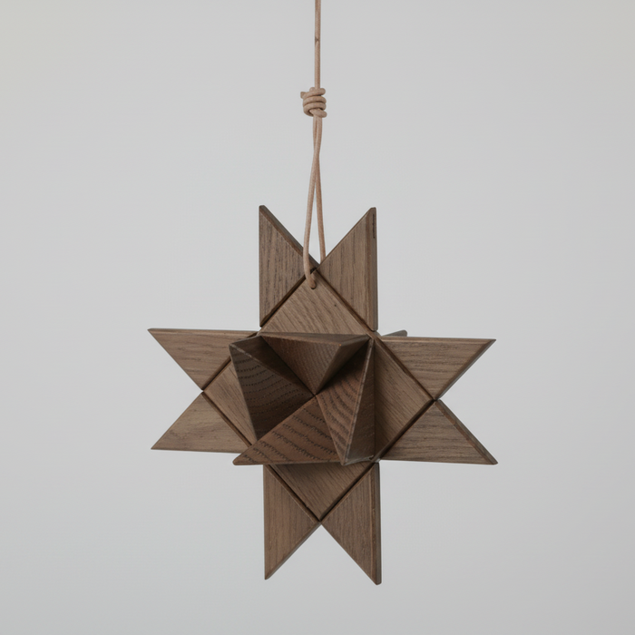 Hanging geometric star ornament crafted from smoked wood, composed of interlocking triangular facets and suspended by a natural cord, showcasing rich dark wood grain and a sculptural matte finish against a plain white background.