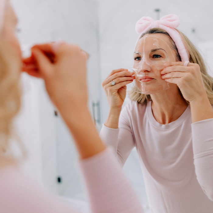Woman applying full face collagen mask in front of a mirror