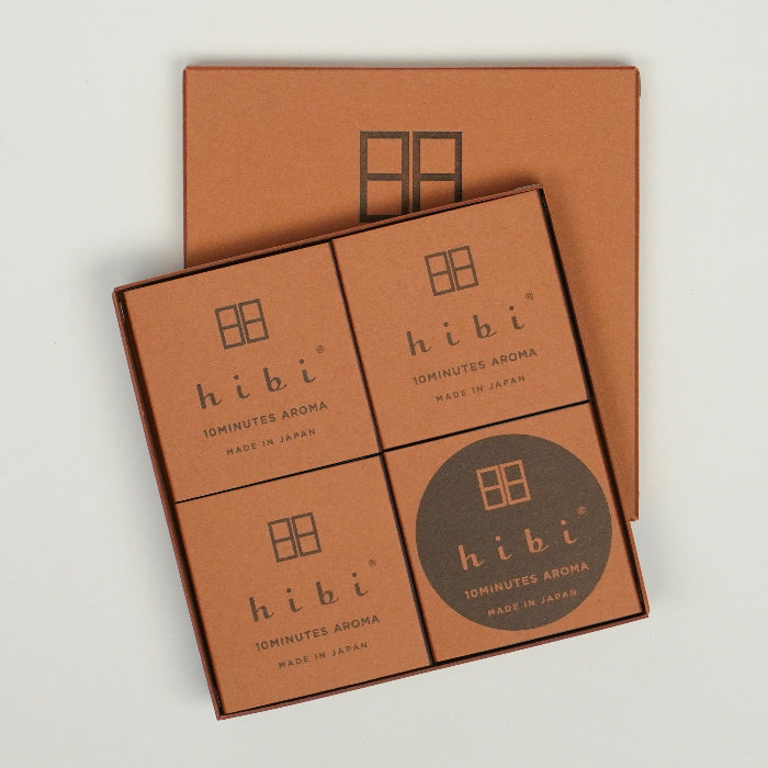An open square hibi 10 Minutes Aroma gift box on a white background, showing four brown minimalist inner boxes arranged in a grid, with the matching brown hibi box lid placed behind the open set.