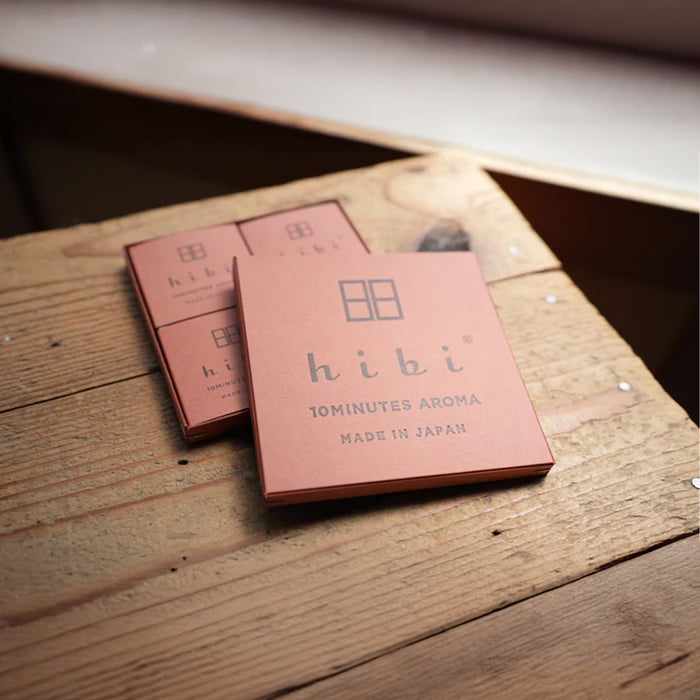 Two hibi 10 Minutes Aroma incense match boxes resting on a rustic wooden surface, with one box slightly overlapping the other, showcasing the minimalist brown packaging and subtle branding in a natural, lifestyle setting.