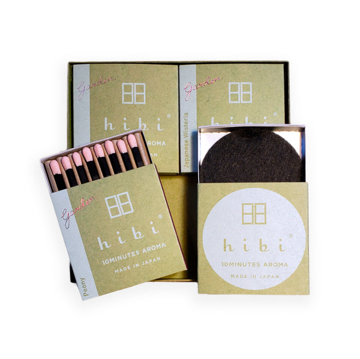An open hibi 10 Minutes Aroma “Garden” gift set on a white background, featuring green-labeled incense match boxes, one opened to show pink-tipped incense matches, and a square holder containing a round black striker pad, arranged to display the contents of the set.