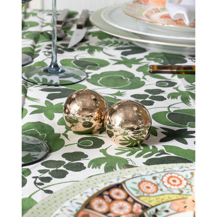 Shiny gold spherical salt and pepper shakers with star cutouts on green and white patterned tablecloth.