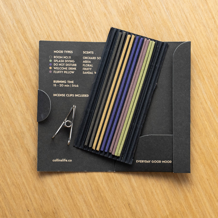 A variety of incense sticks in different colors, displayed in a black packaging with a card that includes the brand name and scent names.