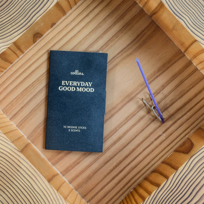 Collins Everyday Good Mood incense stick set with black packaging and a single purple incense stick in a metal holder, styled on a natural wood tray for calm minimalist home fragrance.