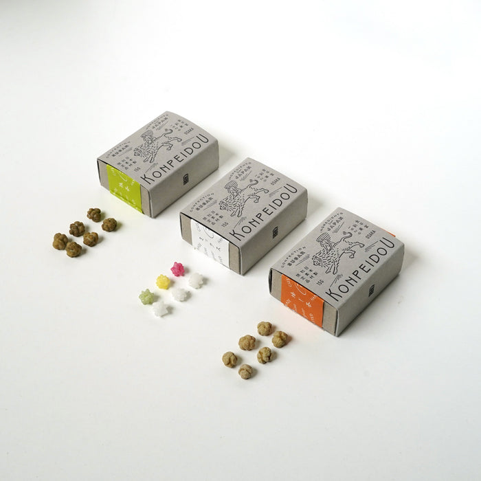 Three small Korpédou boxes arranged on a white background with small batches of brown capsules or beads placed in front of each box. The boxes are light gray with black line drawings and text, and the side tabs are lime green, white, and orange.