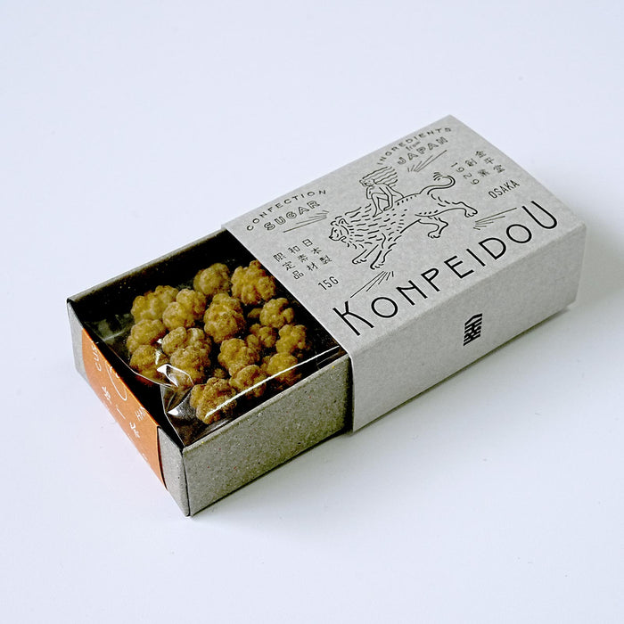 An open kraft paper box of Kompeidou confectionery snacks, showing golden-brown fried snacks inside a clear plastic bag, photographed on a clean white background.