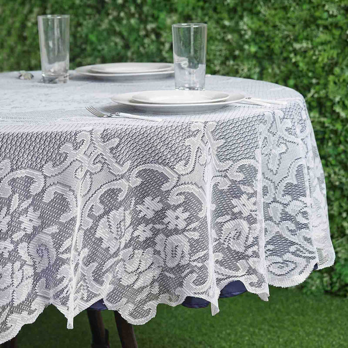 Lace tablecloth draped over a round table set with plates and glasses.