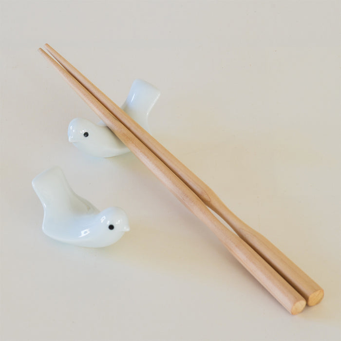 Set of two white bird-shaped ceramic chopstick rests with wooden chopsticks, displayed on a clean neutral background in a minimalist tabletop product presentation.