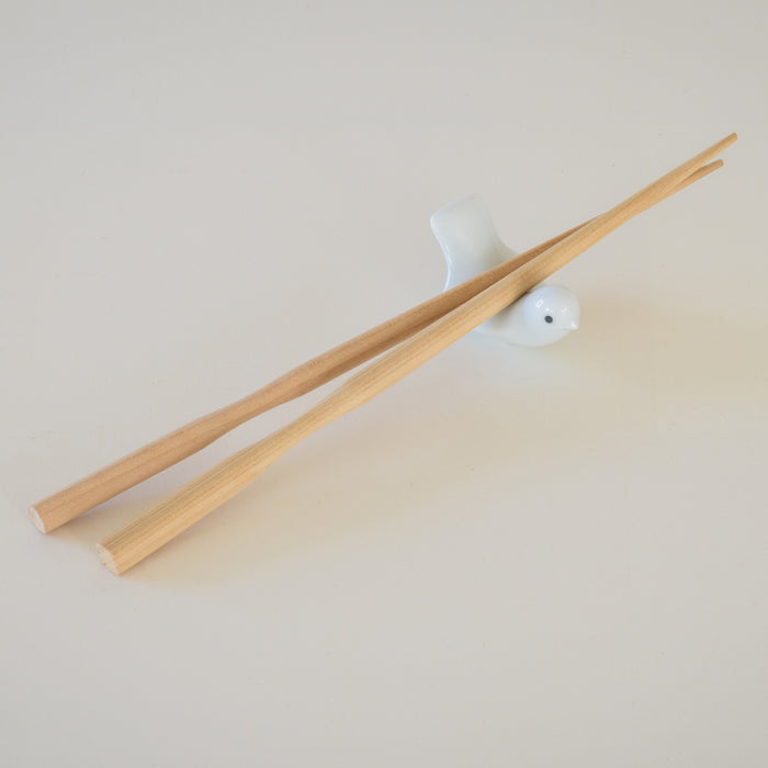 Wooden chopsticks resting on a white bird-shaped ceramic chopstick holder, displayed on a clean neutral background in a minimalist tabletop product presentation.