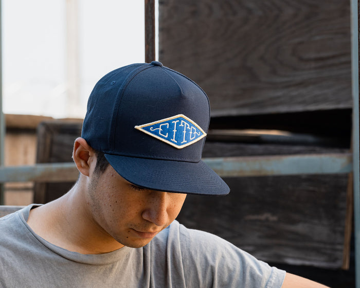 man wearing - blue suavecito hat with white embroidered text and blue background "cito" in diamond shape