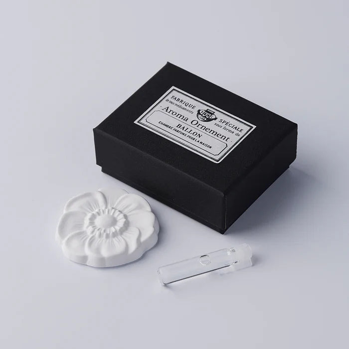 White flower-shaped aroma ornament set with a black vintage-style gift box and small fragrance vial, displayed on a clean white background in a minimalist product presentation.
