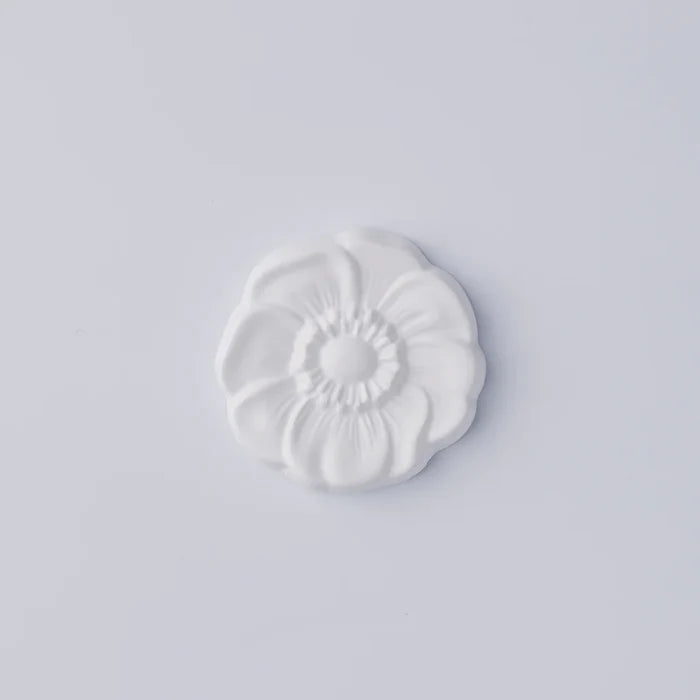 White flower-shaped decorative object with sculpted petals and a raised center, photographed against a clean white background in a minimalist product presentation.