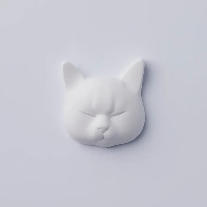 White cat-face decorative object with closed eyes and sculpted feline features, photographed against a clean white background in a minimalist product presentation.