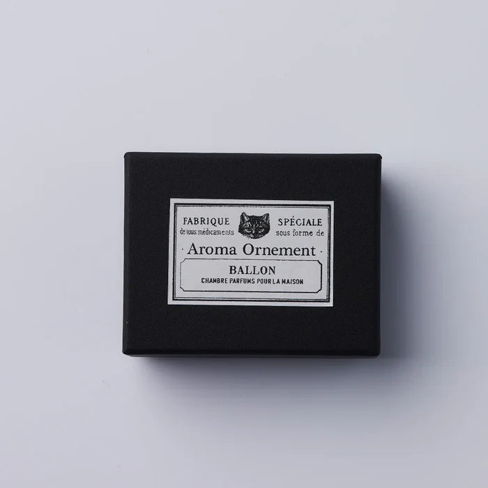 Black Aroma Ornament box with vintage-style label and cat illustration, photographed against a clean white background in a minimalist product presentation.